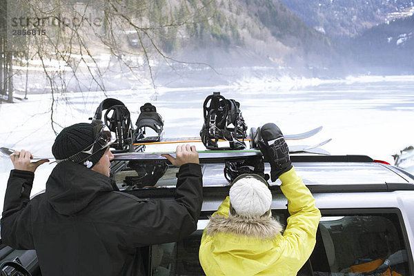 Paar  das Snowboards von Dachgepäckträger nimmt