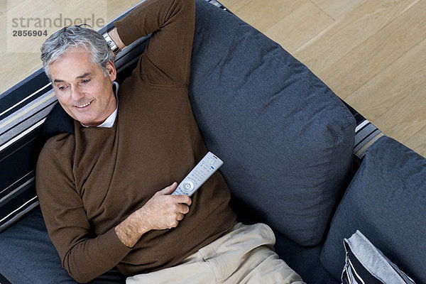 Mann entspannt auf Sofa mit TV-Fernbedienung