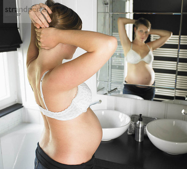 Schwangere Frau schaut in den Spiegel