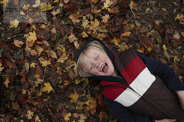 Junge auf Herbstblättern liegend