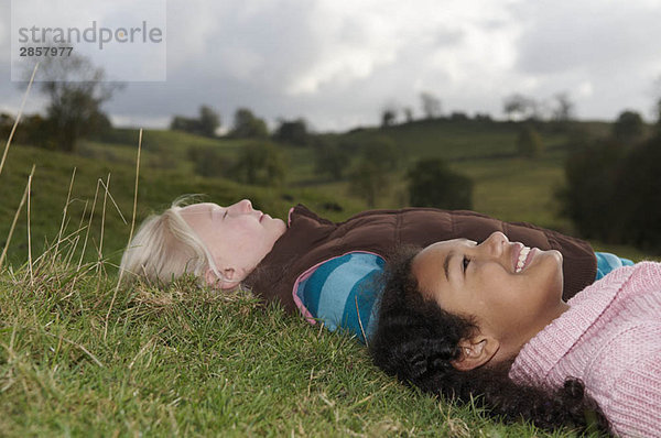 Zwei Mädchen liegen auf Gras und schauen in den Himmel.