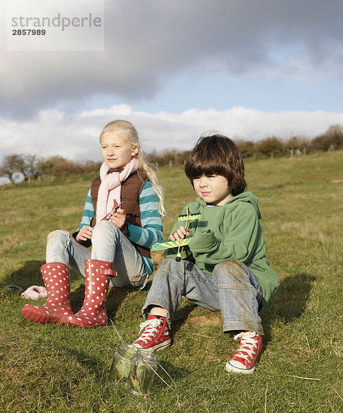 Mädchen und Junge mit Spielzeugflugzeugen im Feld