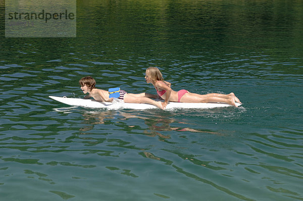 Junge und Mädchen (6-7) auf dem Surfbrett schwimmend auf dem Wasser