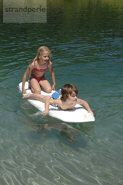 Junge und Mädchen (6-7) auf dem Surfbrett schwimmend auf dem Wasser