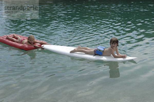 Junge und Mädchen (6-7) auf dem Surfbrett schwimmend auf dem Wasser