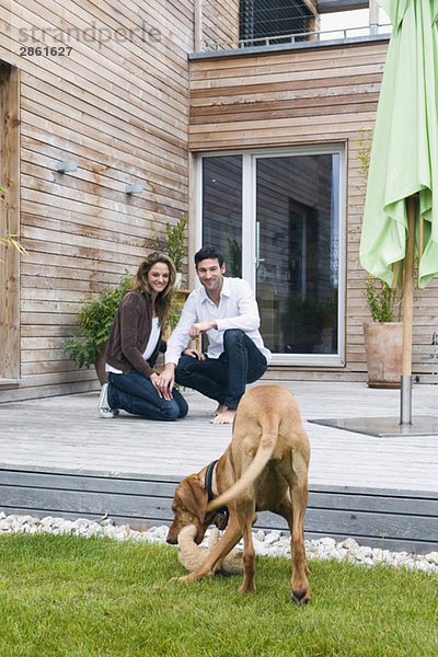 Deutschland  Bayern  München  Paar auf Terrasse vor dem Haus mit Hund