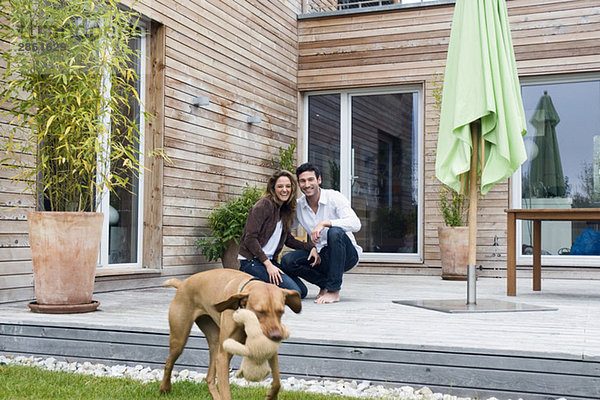 Deutschland  Bayern  München  Paar auf Terrasse vor dem Haus mit Hund