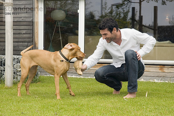 Junger Mann spielt mit Hund im Garten