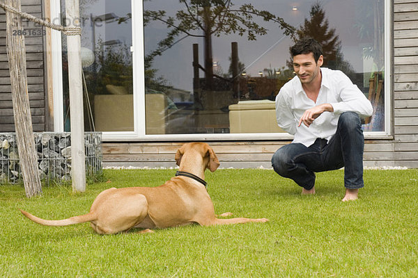 Junger Mann spielt mit Hund im Garten