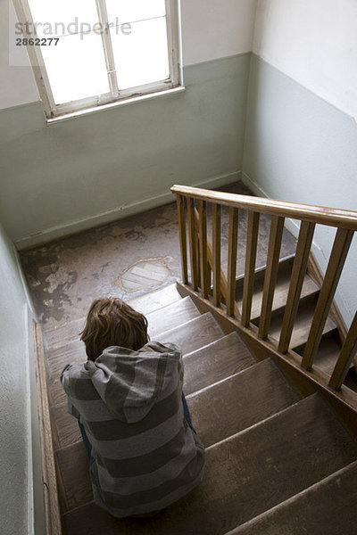 Junge (12 Jahre) sitzend im Treppenhaus  Rückansicht