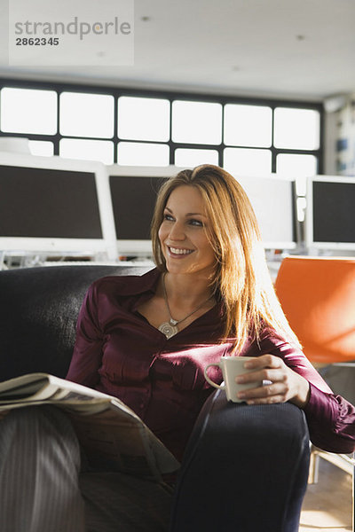 Geschäftsfrau im Büro mit Becher und Zeitung  lächelnd  Portrait