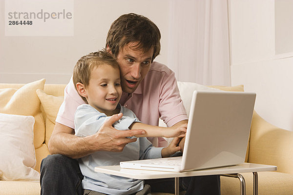 Vater und Sohn (4-5) sitzen auf dem Sofa mit Laptop