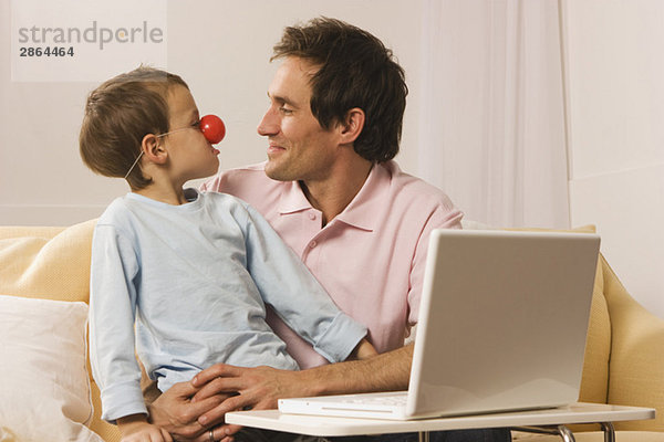 Vater und Sohn (4-5) mit Laptop  Junge mit Clownsnase