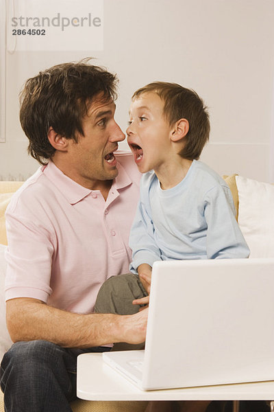 Vater und Sohn (4-5) mit Laptop mit lustigen Gesichtern