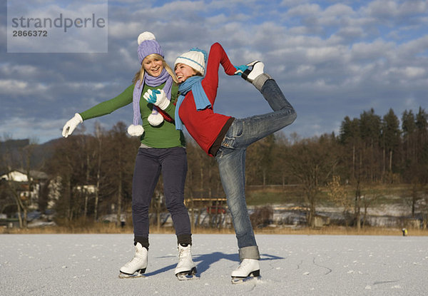 Austria  Salzkammergut  Lake Irrsee  Female teenagers (14-15) skating  one girl stretching leg