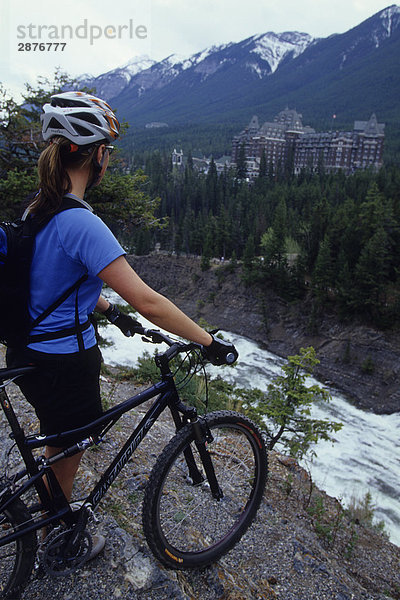 Eine Frau mit ihr Mountainbike genießen die Aussicht im Banff-Nationalpark  Rocky Mountains  Alberta  Kanada. Banff Springs Hotel kann im Hintergrund gesehen werden.