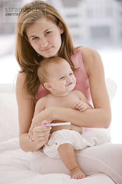 Frau hält einen Schwangerschaftsteststab mit ihrer Tochter auf dem Schoß.