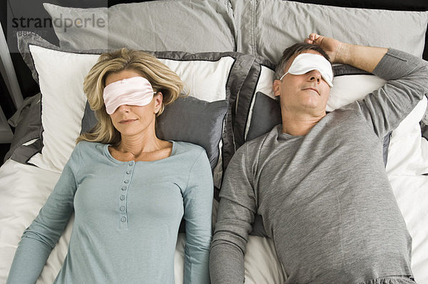 Ein Paar schläft im Bett und trägt eine Augenmaske.