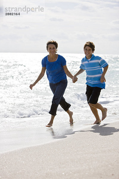 Frau läuft mit ihrem Enkel am Strand entlang