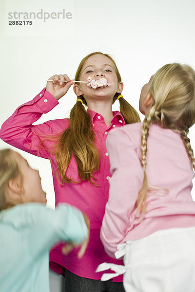 Mädchen  das einen Lolli isst und ihre Freunde  die sie ansehen.