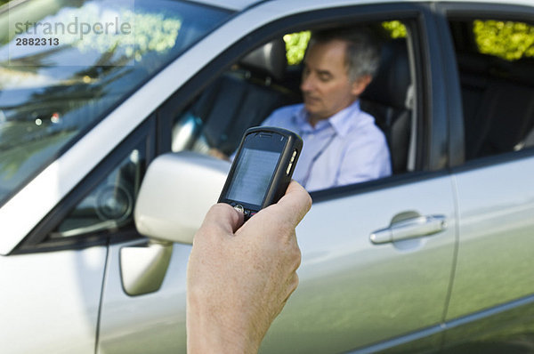 Hand-SMS und ein Mann  der im Hintergrund in einem Auto sitzt.