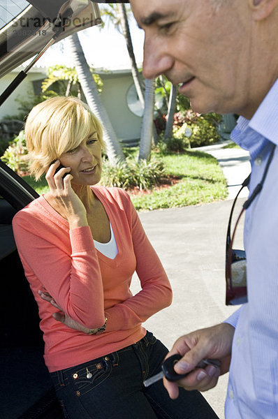 Mann hält einen Autoschlüssel neben einer Frau  die auf einem Handy spricht