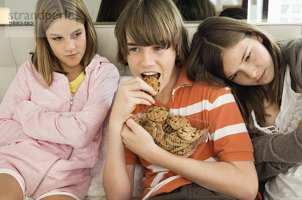 Junge isst Schokokekse mit zwei Mädchen neben ihm