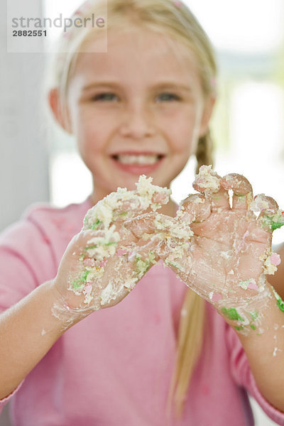 Porträt eines Mädchens  das seine unordentliche Hand mit Kuchenglasur bedeckt zeigt.