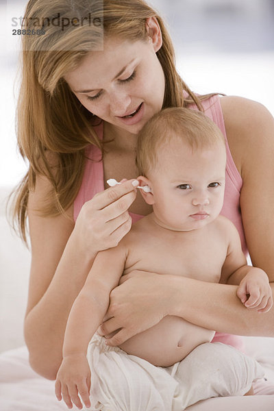 Frau reinigt das Ohr ihrer Tochter mit einem Wattestäbchen