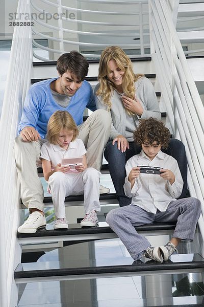 Eltern sitzen mit ihren Kindern auf der Treppe und spielen Videospiele.