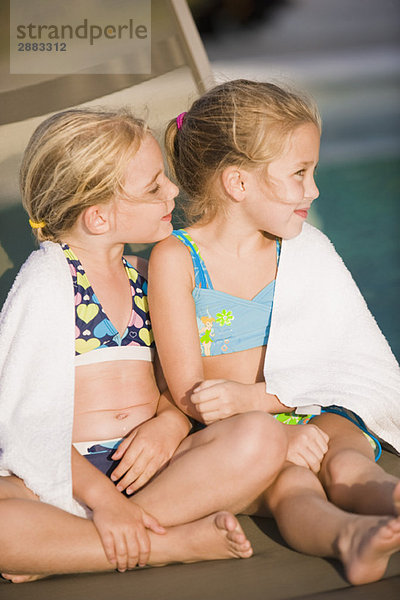 Zwei Mädchen sitzen auf einem Liegestuhl am Pool