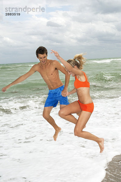 Paar beim Händchenhalten und Springen am Strand