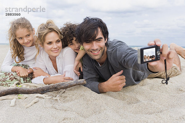 Ein Mann fotografiert seine Familie mit einer Digitalkamera am Strand.