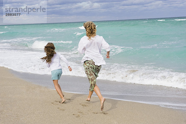 Frau läuft mit ihrer Tochter am Strand.