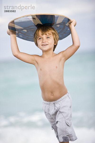 Junge hält ein Bodyboard über den Kopf.