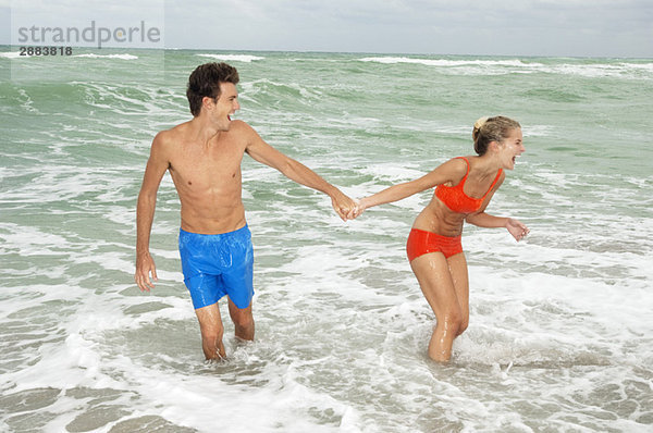 Paar hält sich an den Händen und geht im Wasser am Strand spazieren.