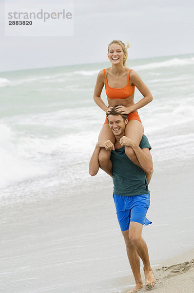 Mann  der eine Frau auf seinen Schultern am Strand trägt.