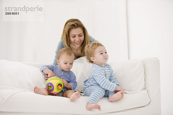 Frau spielt mit ihrem Sohn und ihrer Tochter auf einer Couch.