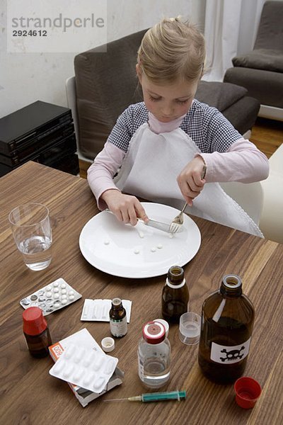 Ein junges Mädchen schneidet eine Pille  umgeben von Medikamenten.