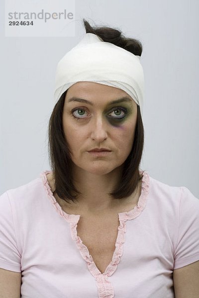 Eine Frau mit einem blauen Auge und bandagiertem Kopf.