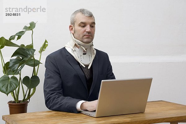 Ein Geschäftsmann mit einer Halskrause  der an einem Laptop arbeitet.