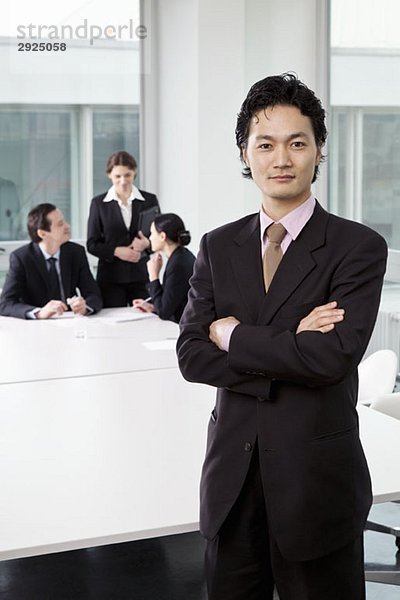 Porträt eines Geschäftsmannes in einem Vorstandszimmer mit unscharfen Geschäftsleuten im Hintergrund