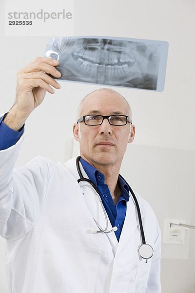 Ein Zahnarzt hält ein Röntgenbild hoch.