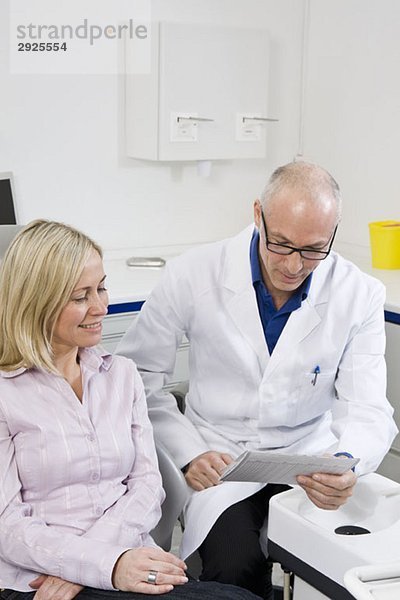 Ein Zahnarzt im Gespräch mit einem Patienten  der auf einem Zahnarztstuhl sitzt.