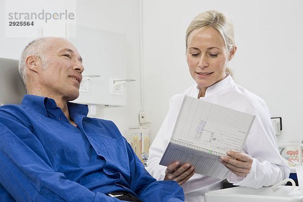 Ein Zahnarzt im Gespräch mit einem Patienten  der auf einem Zahnarztstuhl sitzt.