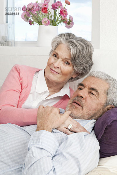 Ein älterer Mann und eine ältere Frau liegen zusammen auf einer Couch.