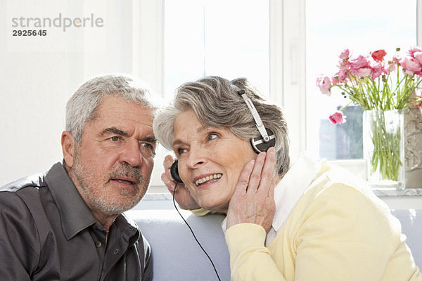 Eine ältere Frau  die ihre Kopfhörer teilt  damit ein älterer Mann zuhören kann.