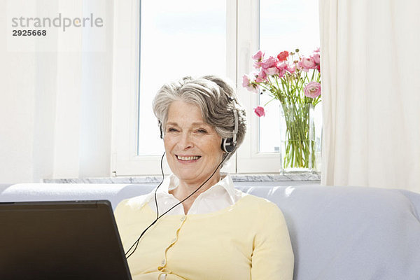 Eine Frau  die einen Laptop benutzt und Kopfhörer hört.