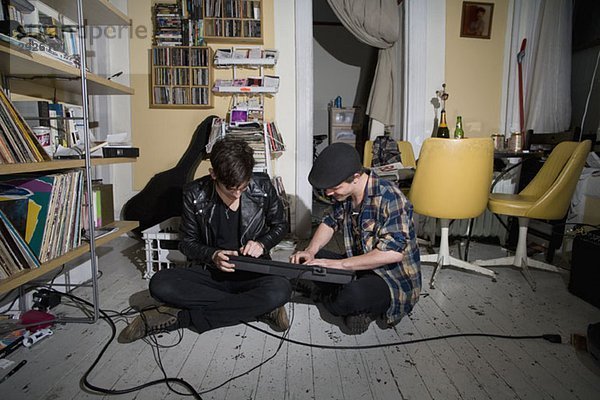 Zwei junge Männer sitzen auf dem Boden und spielen Keyboard.
