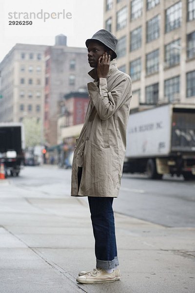 Ein junger Mann  der auf einem Bürgersteig steht und ein Handy benutzt.